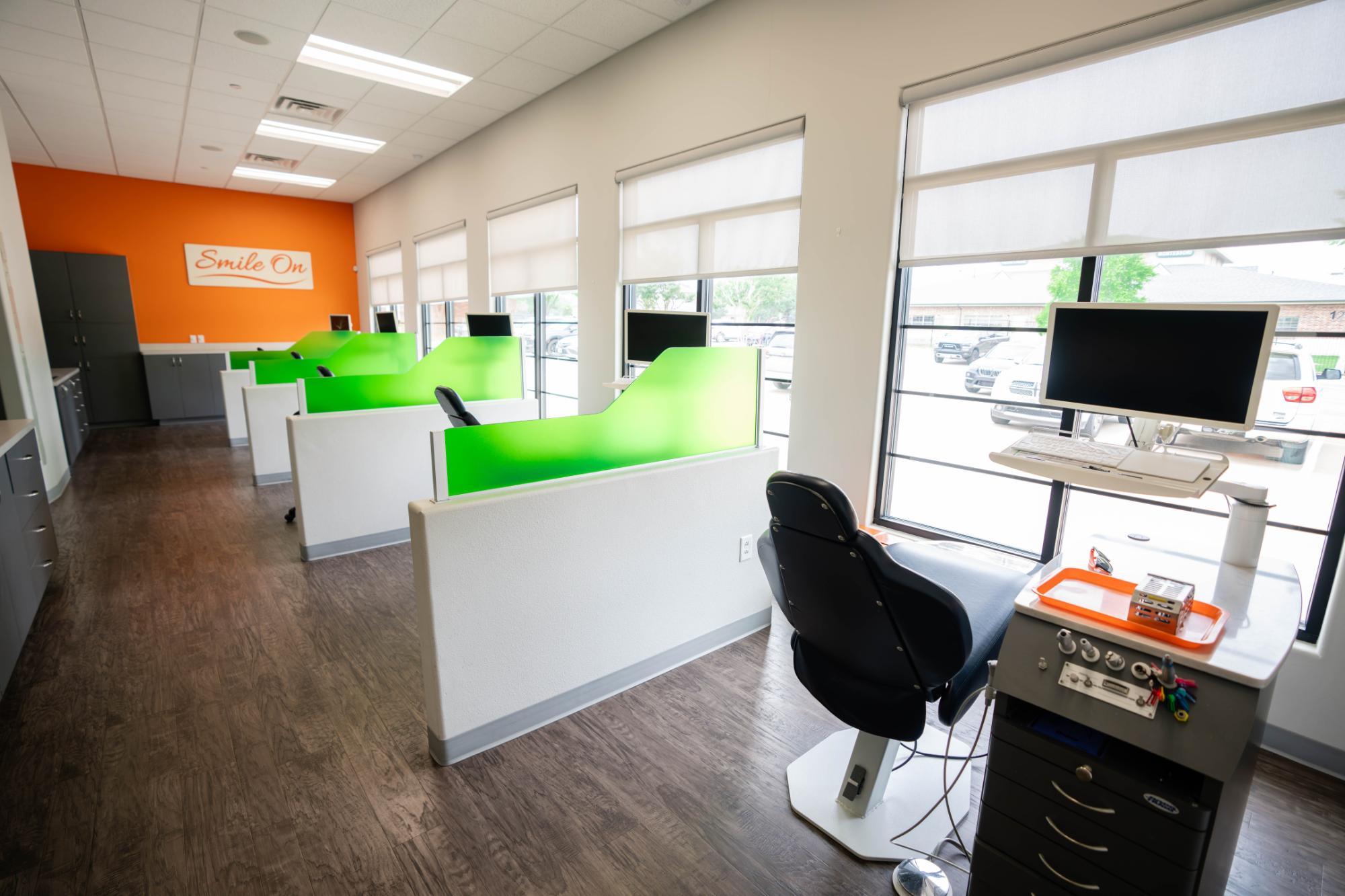 Welcoming orthodontic office interior with green partitions, modern dental chair, and "Smile On" sign, reflecting a friendly and comfortable environment for patients at Kraus Orthodontics.