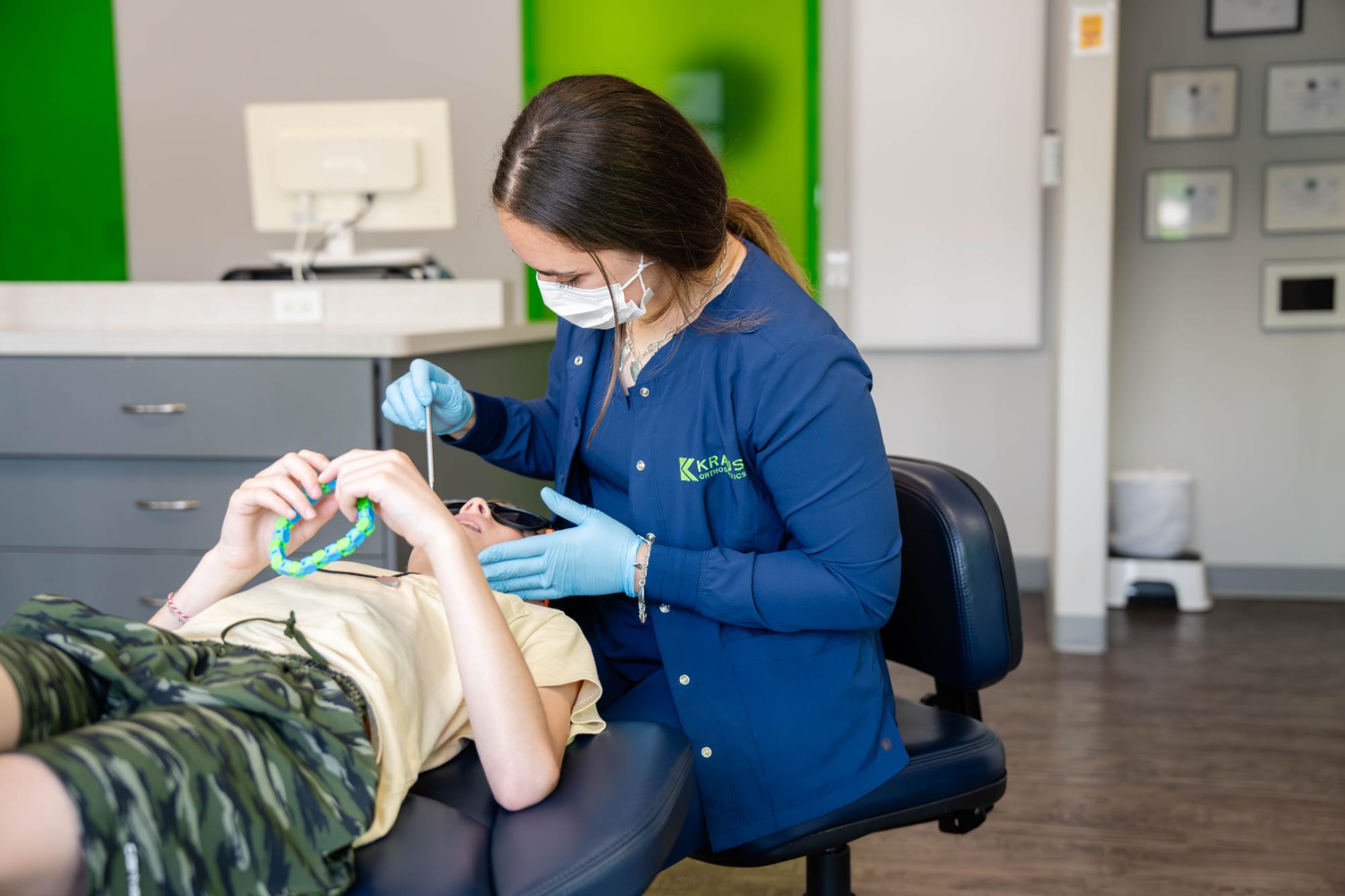 Orthodontic treatment session at Kraus Orthodontics, featuring a dental professional in a blue coat assisting a young patient with braces, highlighting the comfortable and advanced care environment.
