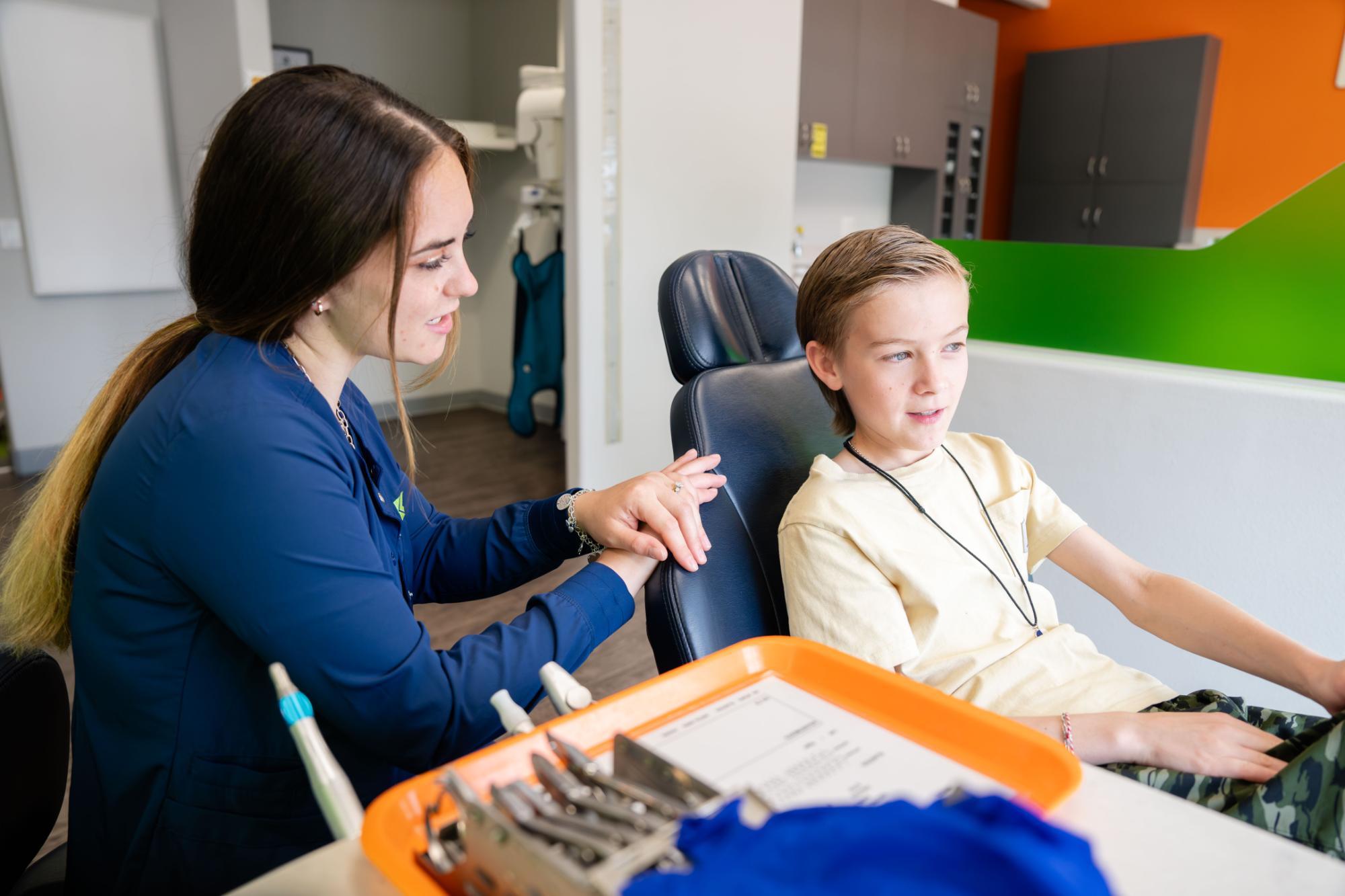 Orthodontic consultation scene with a dental professional interacting with a young patient, showcasing a friendly environment at Kraus Orthodontics, with dental tools and paperwork in view.