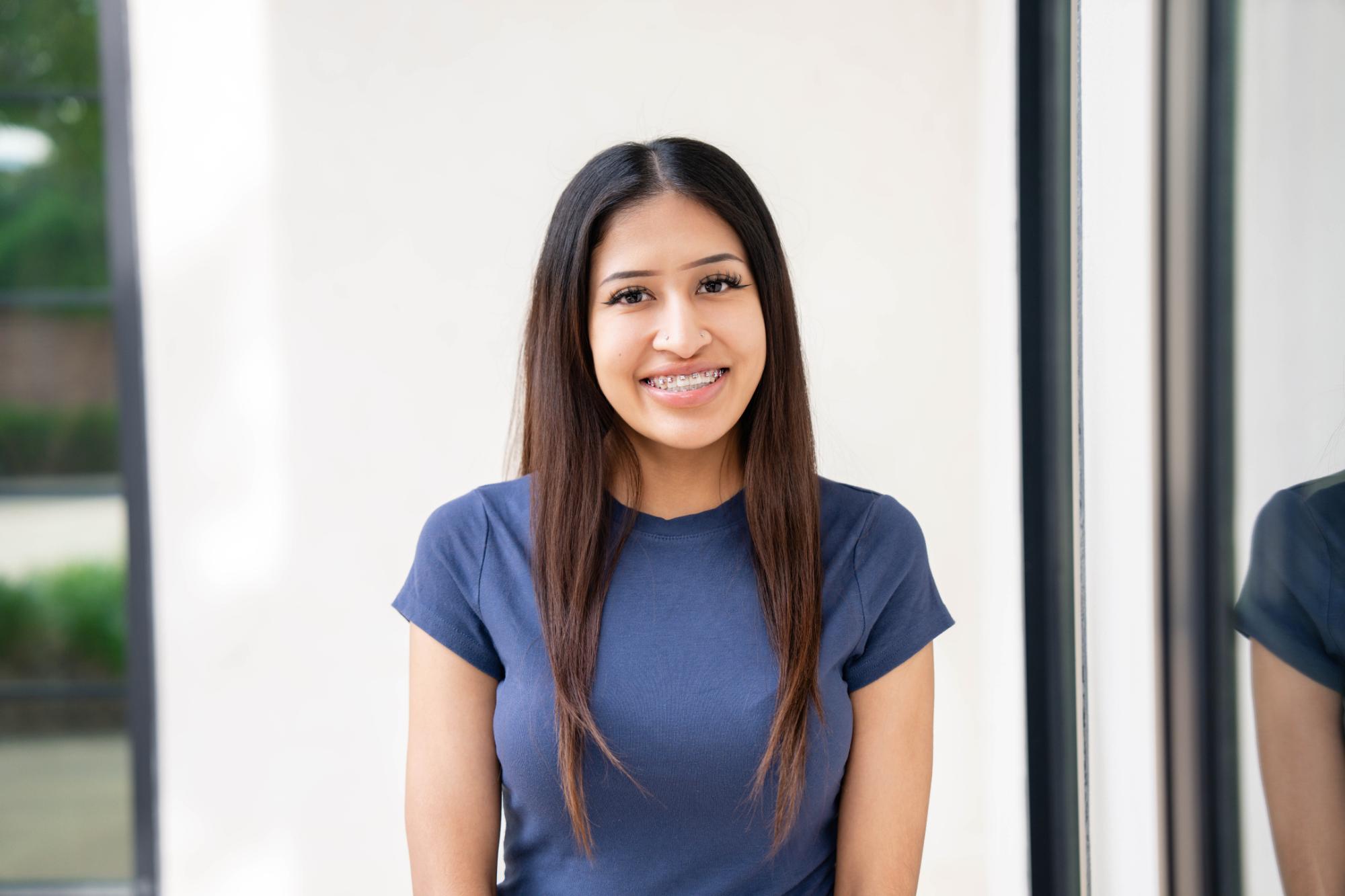 Smiling young woman with metal braces wearing a navy shirt, showcasing a confident smile in a bright, modern orthodontic office setting.