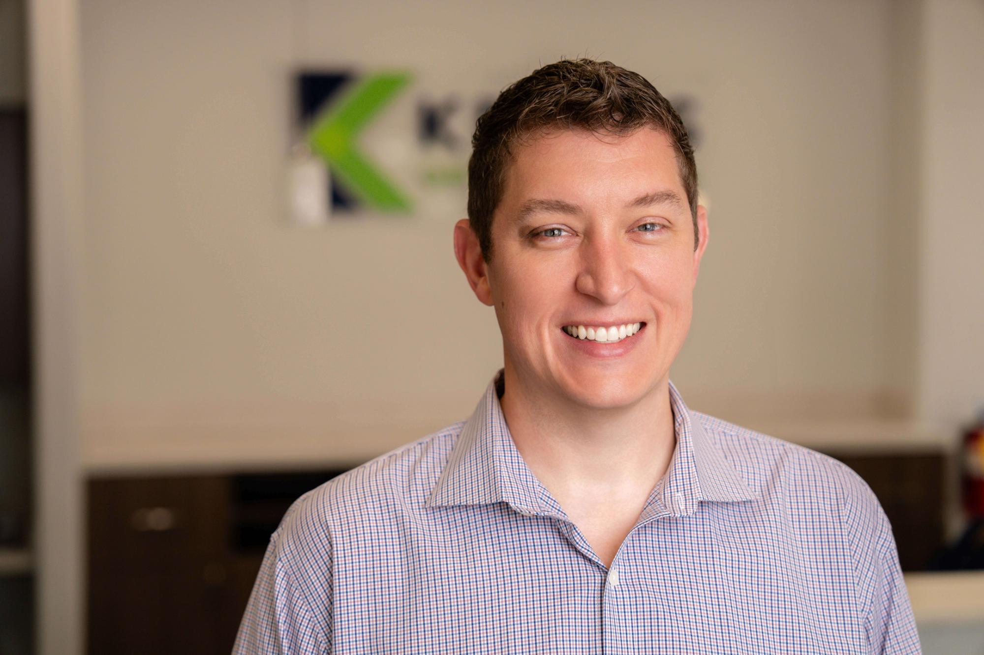 Smiling orthodontist in a professional setting, showcasing Kraus Orthodontics branding in the background, emphasizing personalized care for adult orthodontic treatment.