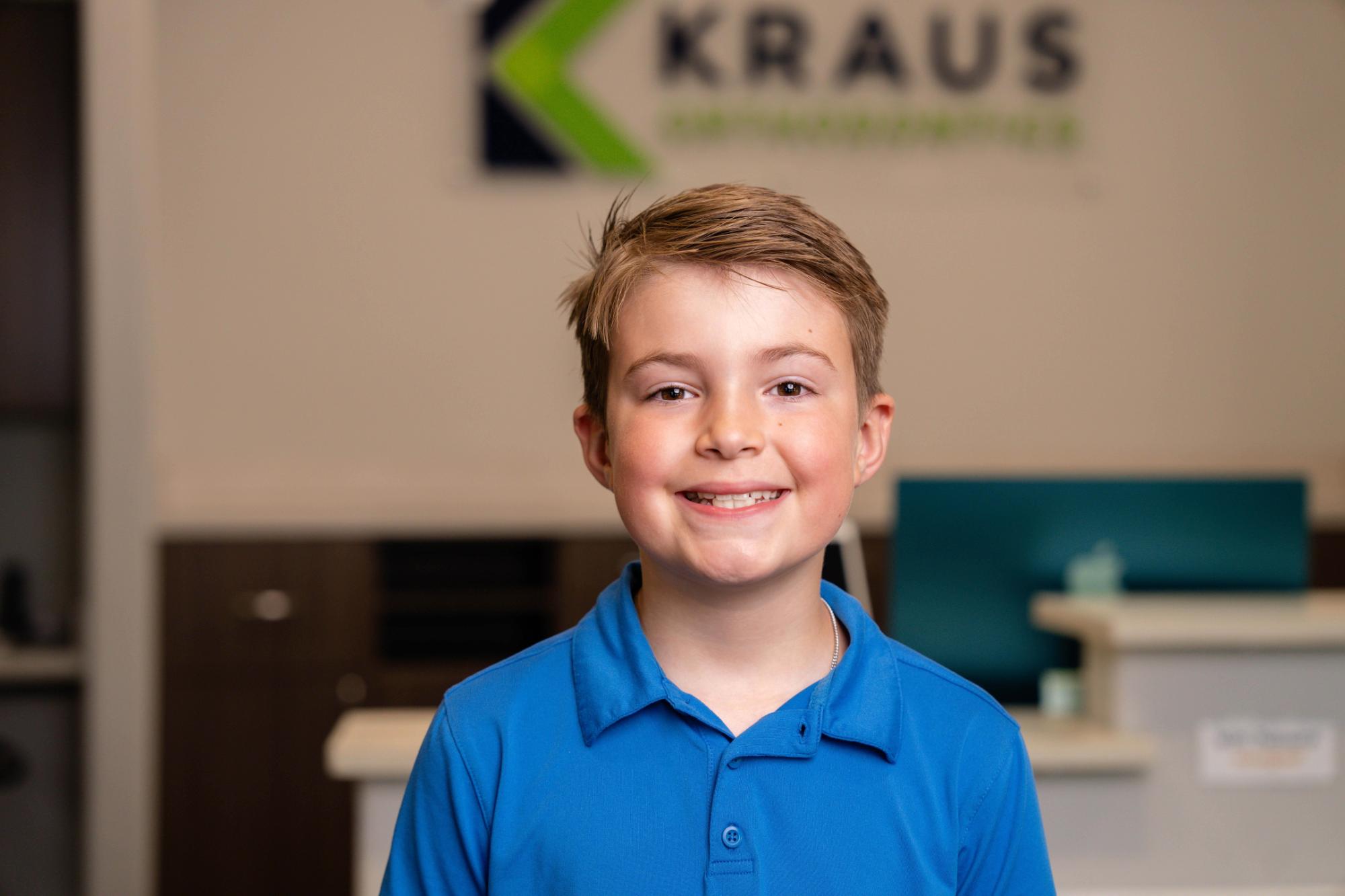 Smiling young boy in a blue shirt at Kraus Orthodontics office, promoting confidence in children's orthodontic care.