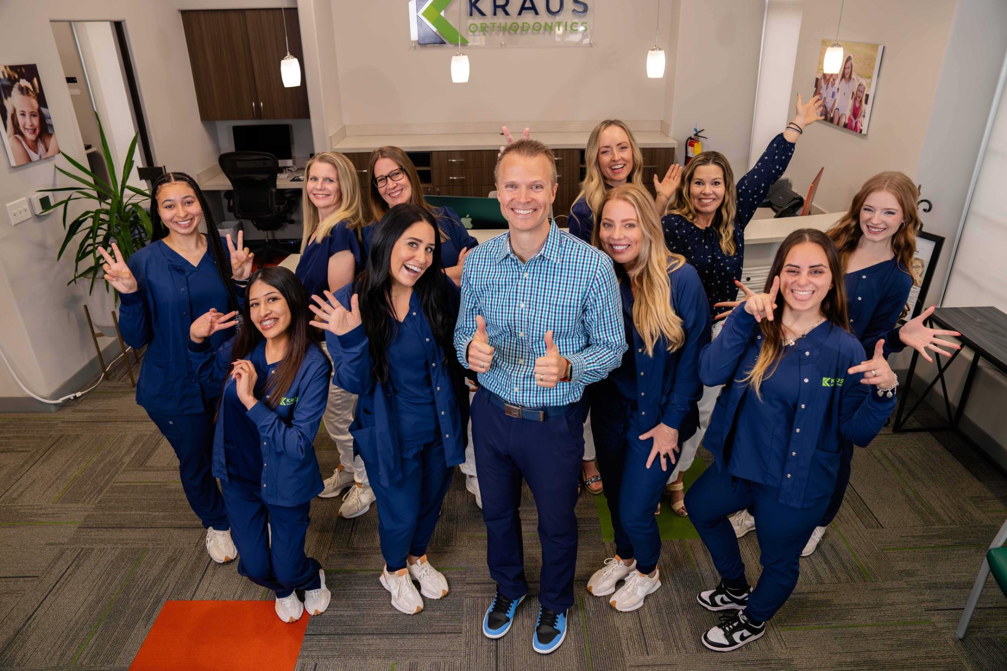 Kraus Orthodontics team smiling and posing together in their office, showcasing a friendly atmosphere and commitment to patient care, emphasizing clear aligner treatment.