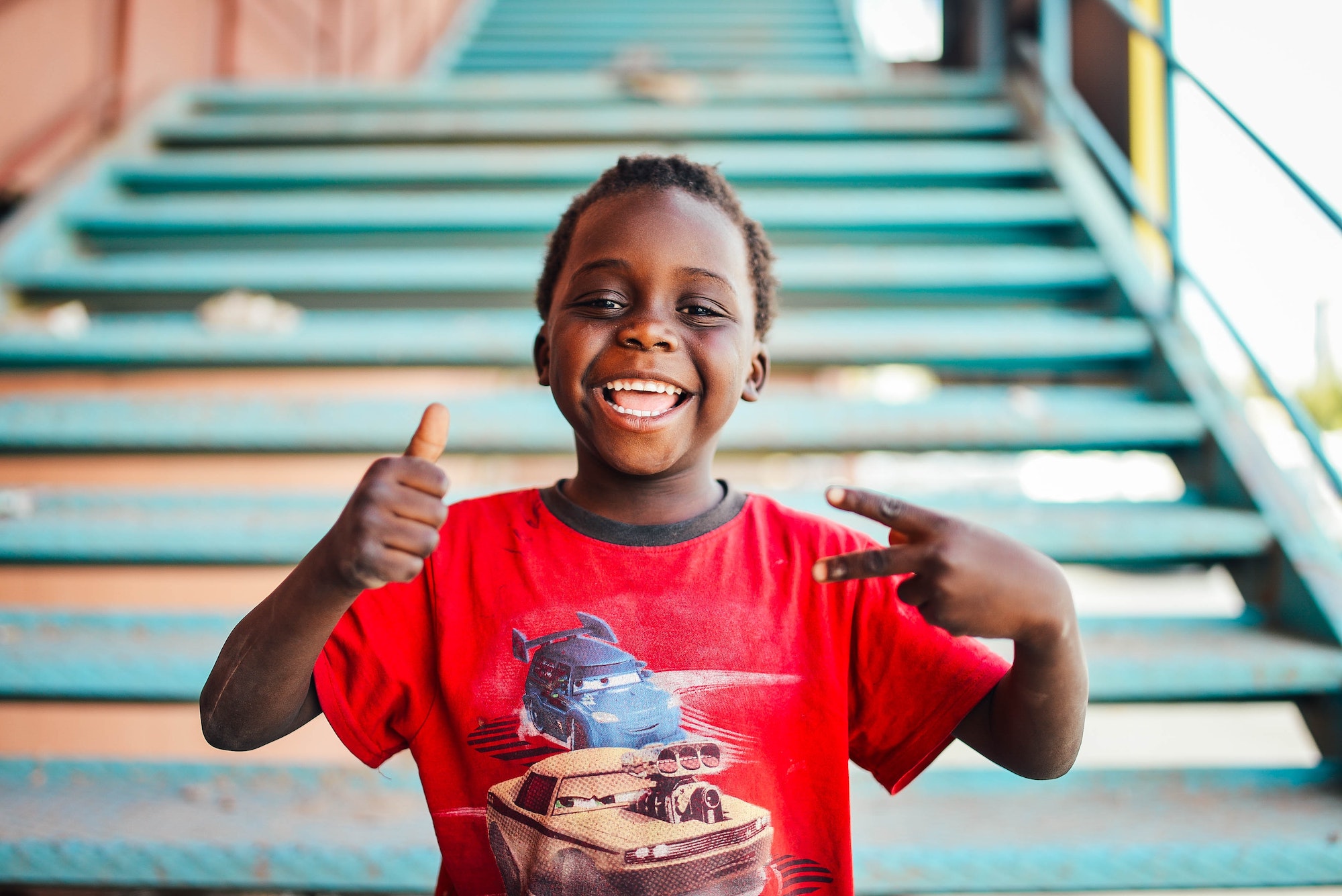 Smiling child in red shirt giving thumbs up and peace sign, representing positive experiences with braces and orthodontics in Allen, encouraging early orthodontic evaluations at Kraus Orthodontics.