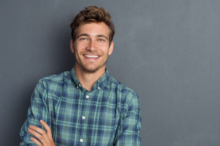 Smiling young man in a plaid shirt, showcasing a confident smile, representing successful orthodontic treatment at Kraus Orthodontics in Allen, TX, emphasizing clear aligners and Invisalign options.