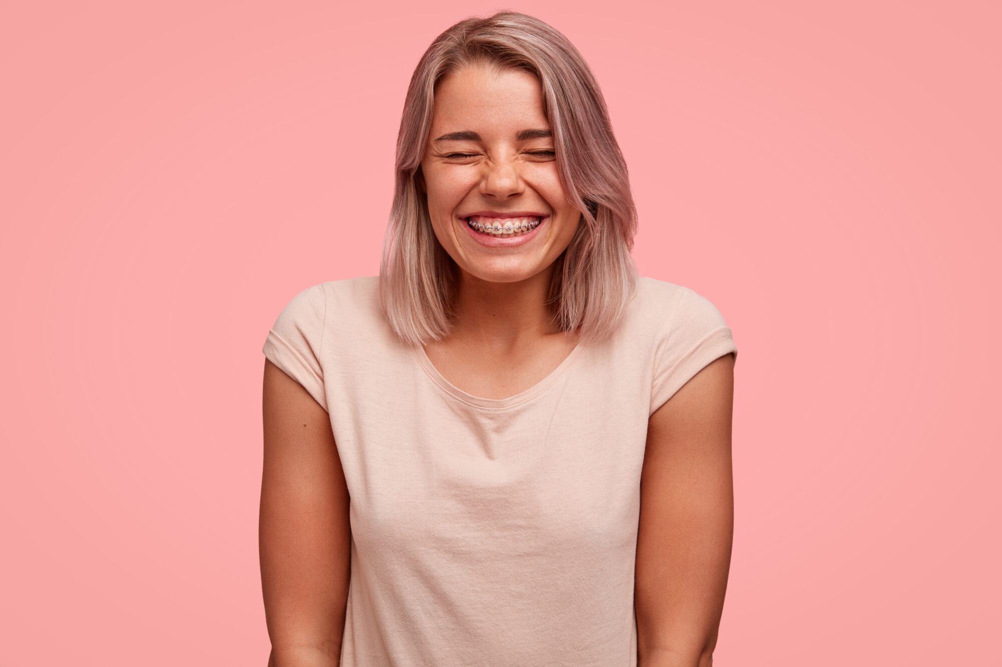 Smiling young woman with braces against a pink background, representing orthodontic treatment options like braces and Invisalign in Allen, TX.