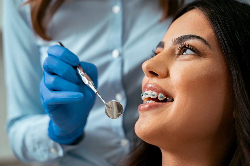 Young woman with braces smiling at an orthodontist in a dental office, showcasing orthodontic care related to braces and clear aligners in Allen, TX.