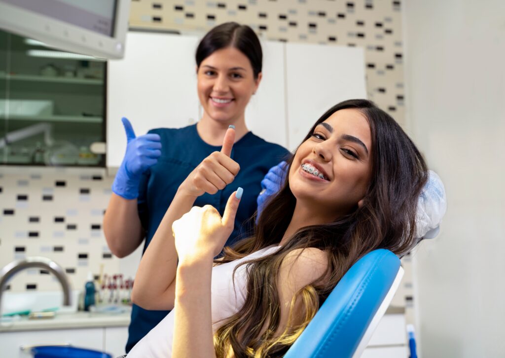 Smiling patient with braces giving a thumbs up alongside an orthodontist in a modern dental office, promoting confidence in orthodontic treatment options like Invisalign in Allen, TX.