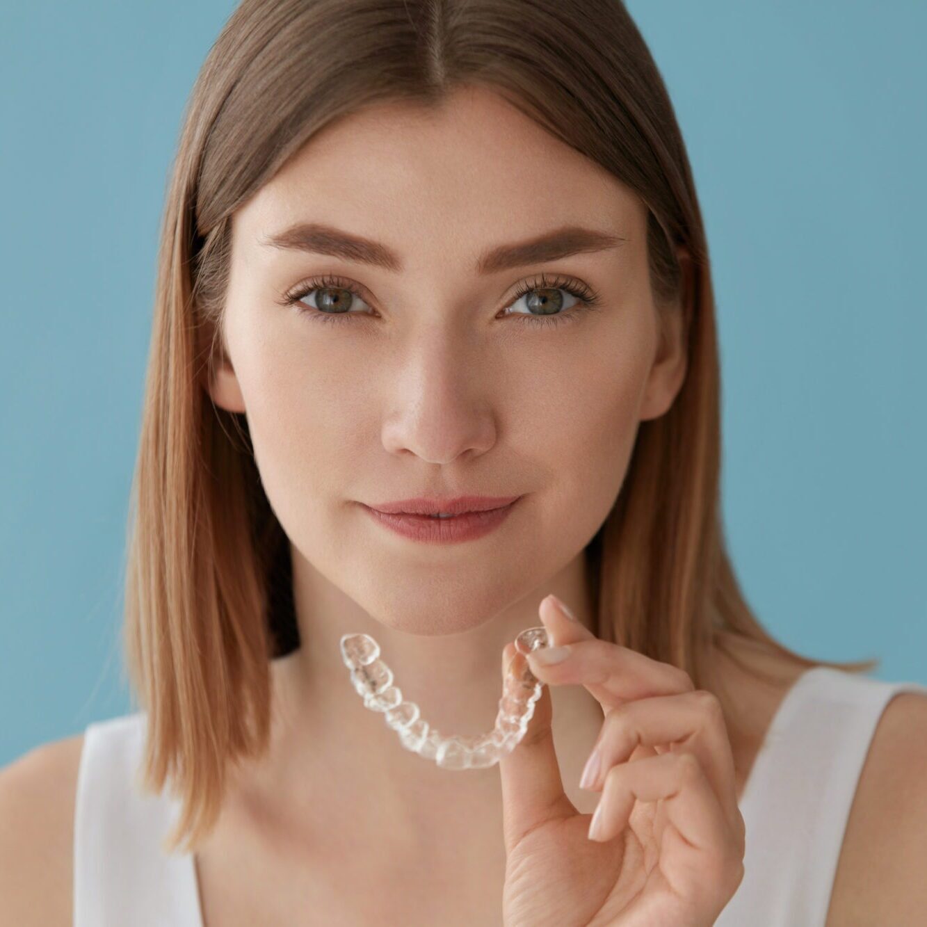 Woman holding clear aligners against a blue background, representing discreet orthodontic treatment options at Kraus Orthodontics in Allen, TX for achieving confident smiles without traditional braces.