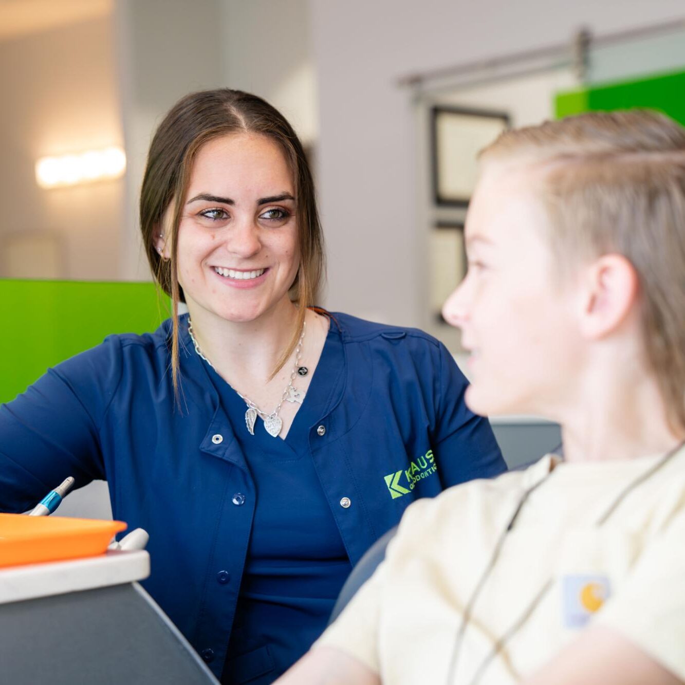Orthodontic assistant smiling and interacting with a young patient in a modern office setting at Kraus Orthodontics, emphasizing personalized care and a welcoming atmosphere.